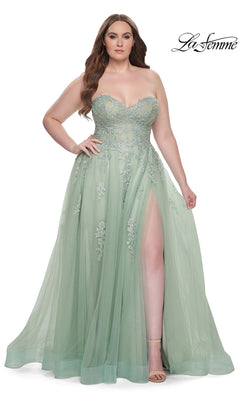 A woman wears the La Femme Long Prom Dress 31570, a plus-size light green strapless gown with floral embroidery, a sheer overlay, and a thigh-high slit, posing against a white background.