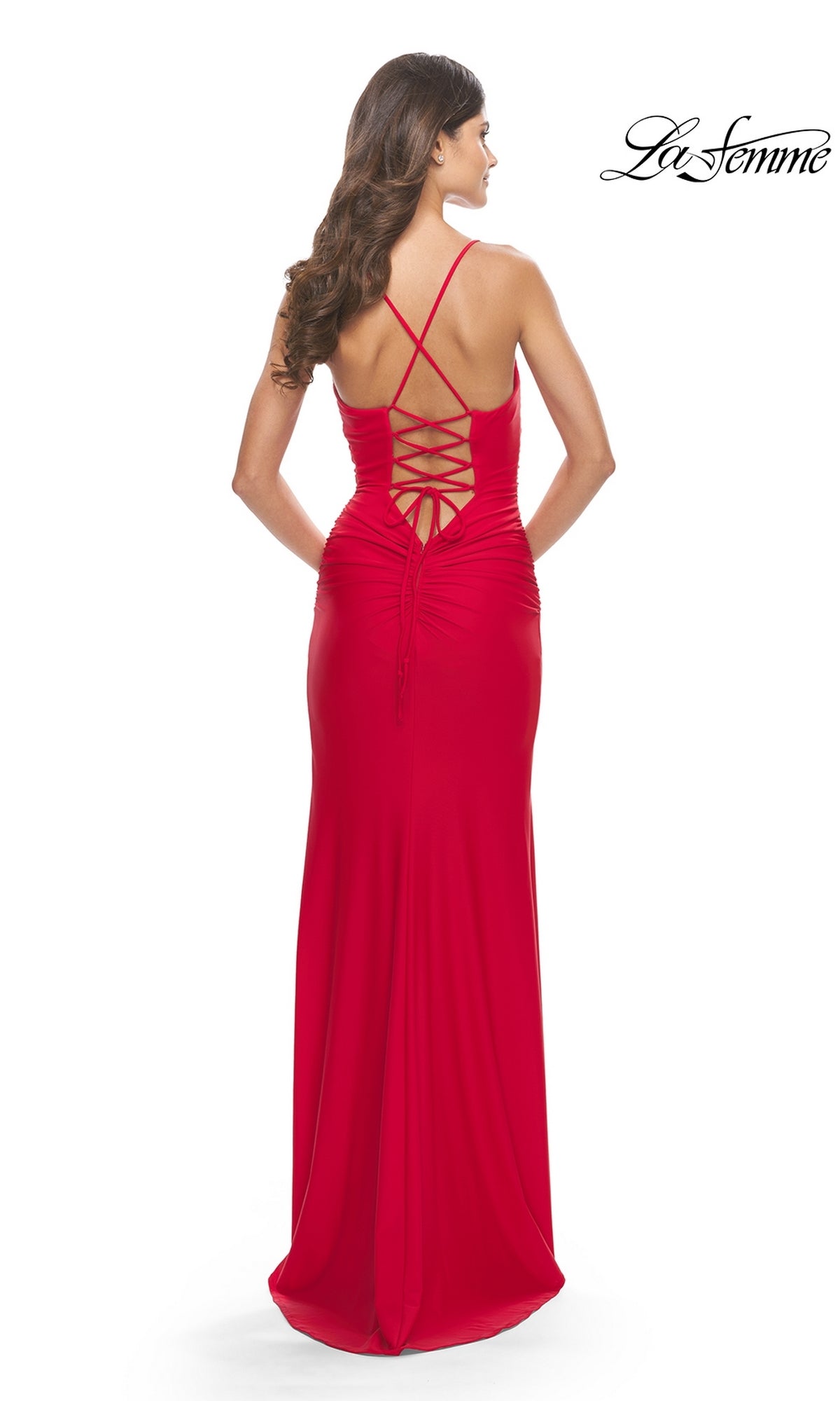 A woman wears the La Femme 31572 Lace-Up Long Ruched Prom Dress, a fitted red gown featuring thin straps, an open lace-up back, and a chic silhouette—perfect for prom—as she stands facing away from the camera.