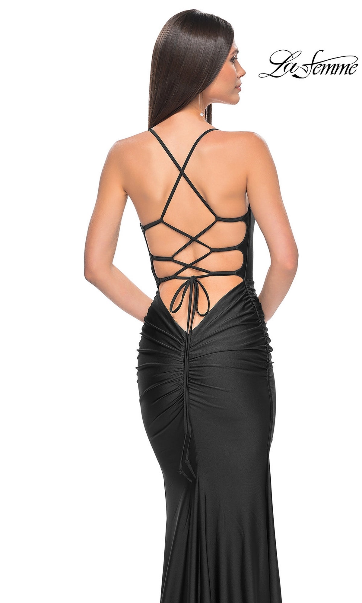 A woman wears the La Femme Strappy-Back Simple Long Prom Dress 31618 in black, featuring a form-fitting silhouette, open back with crisscross lace-up straps, gathered detailing, and the La Femme logo in the top right corner.