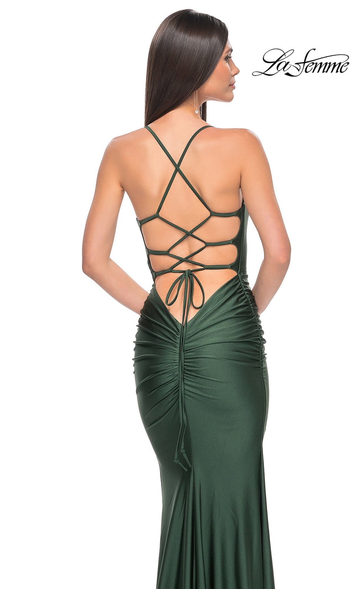 A woman models the La Femme Strappy-Back Simple Long Prom Dress 31618 in dark green, featuring a ruched back and crisscross lace-up straps. This open-back evening gown showcases elegant, eye-catching details for prom night.