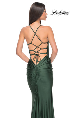 A woman models the La Femme Strappy-Back Simple Long Prom Dress 31618 in dark green, featuring a ruched back and crisscross lace-up straps. This open-back evening gown showcases elegant, eye-catching details for prom night.