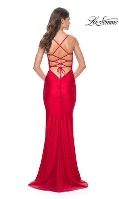 A woman stands facing away in a floor-length La Femme Strappy-Back Simple Long Prom Dress 31618, featuring a bright red hue, open back with strappy detailing, and ruched accents.