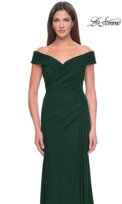 A woman stands against a white background wearing the elegant La Femme Off-the-Shoulder Long Prom Dress 31677 in dark green, featuring ruched detailing. The "La Femme" logo appears in the upper right corner, highlighting timeless style.