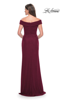 A woman is shown from the back in the La Femme Off-the-Shoulder Long Prom Dress 31677, a floor-length burgundy gown with a fitted bodice and zipper closure, set against a white background for an elegant look.