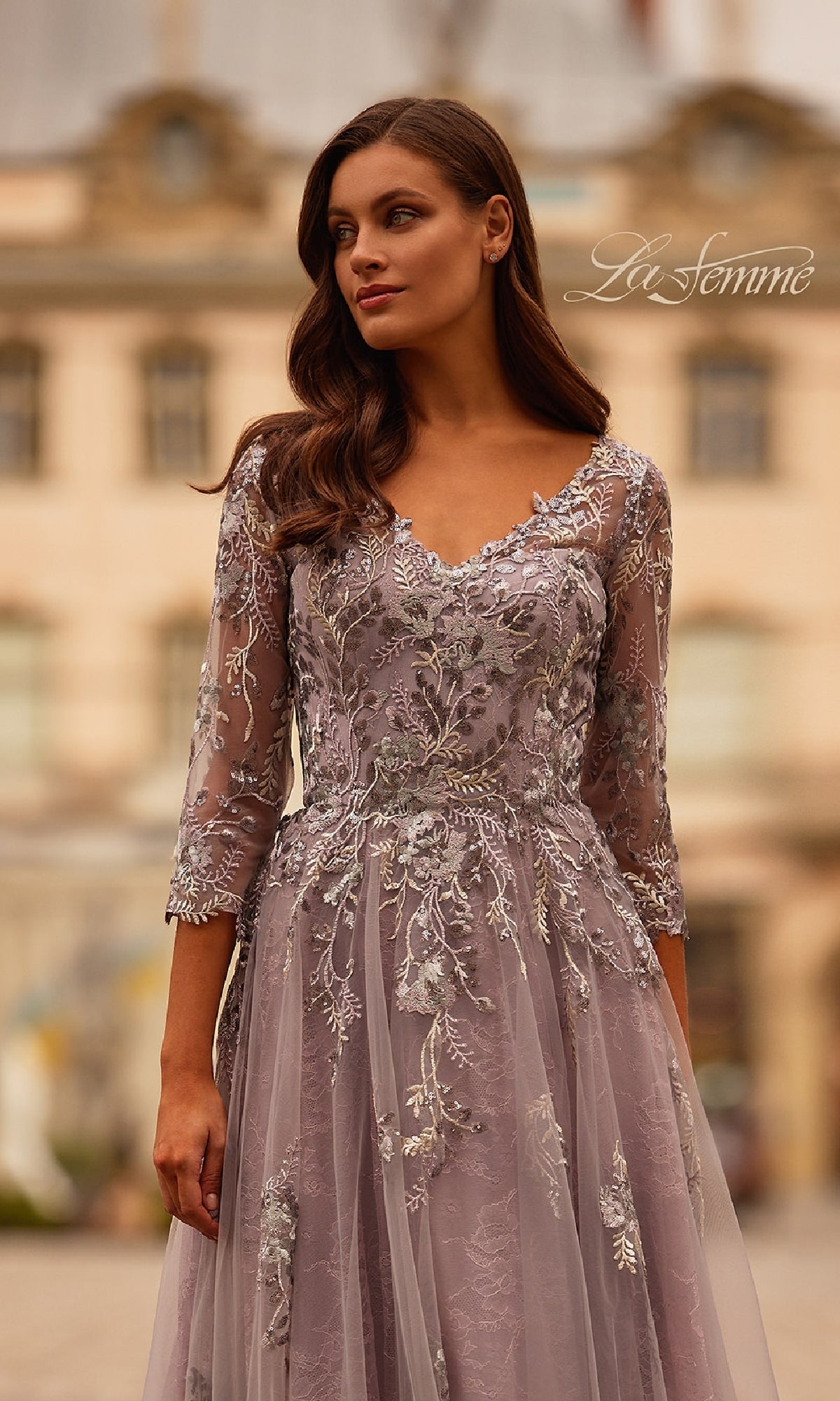 A woman in the Long Sleeve Mauve Formal Gown, La Femme 31717, stands outdoors in front of a blurred building.