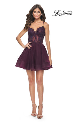A woman wears the Sheer-Bodice Short La Femme Homecoming Dress 31769 in deep purple, featuring a lace corset bodice, spaghetti straps, and flared skirt. She has long wavy brown hair, nude heels, and the La Femme logo appears in the corner.