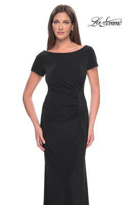 A woman wearing a black short-sleeved La Femme 31773 formal dress with a side-ruched waist and subtle rhinestone embellishments.