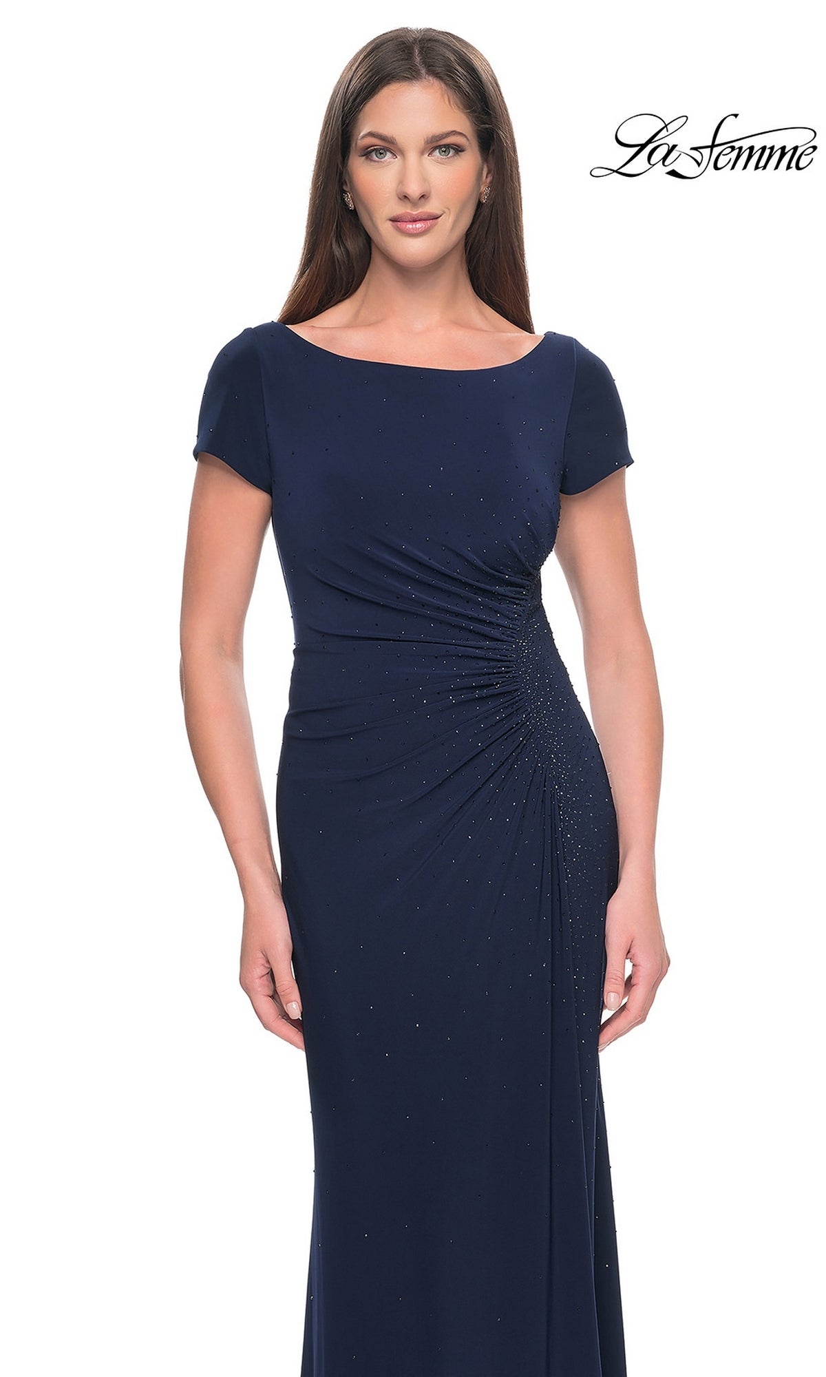 A woman wears a navy blue, short-sleeved rhinestone La Femme 31773 formal dress with a gathered waist and subtle embellishments.