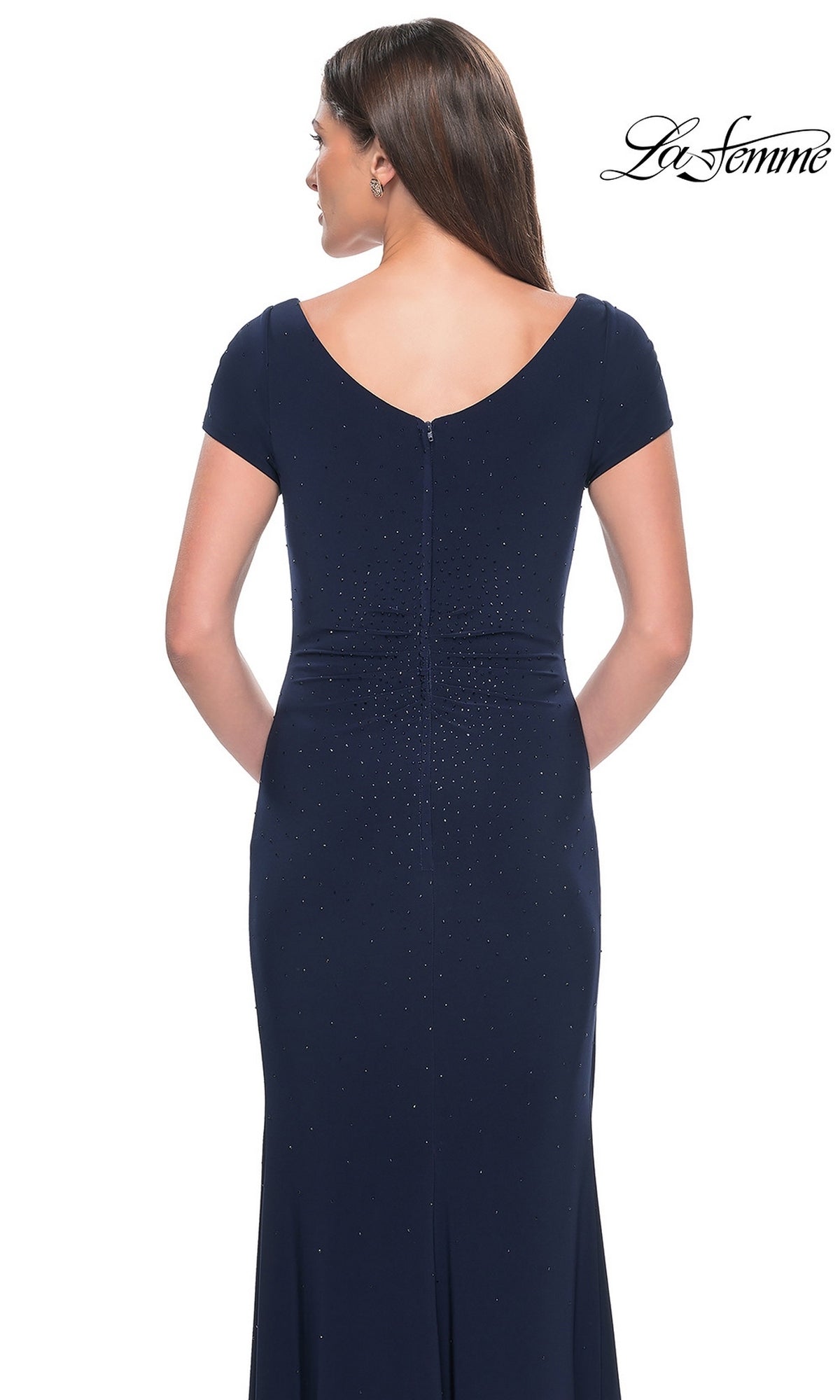 Back view of a woman wearing a dark blue, short-sleeved rhinestone La Femme 31773 formal dress with a v-neck and scattered bead embellishments.