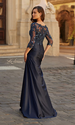 A woman in the La Femme 31802 long formal dress, featuring a satin finish with a beaded lace bodice and sequin accents, stands on a cobblestone street facing away from the camera.