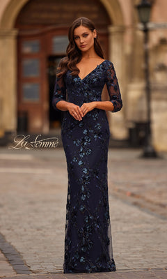 A woman stands outdoors wearing the La Femme 31836 navy blue sequin-lace formal dress, featuring a floor-length design, three-quarter sleeves, and a V-neckline.