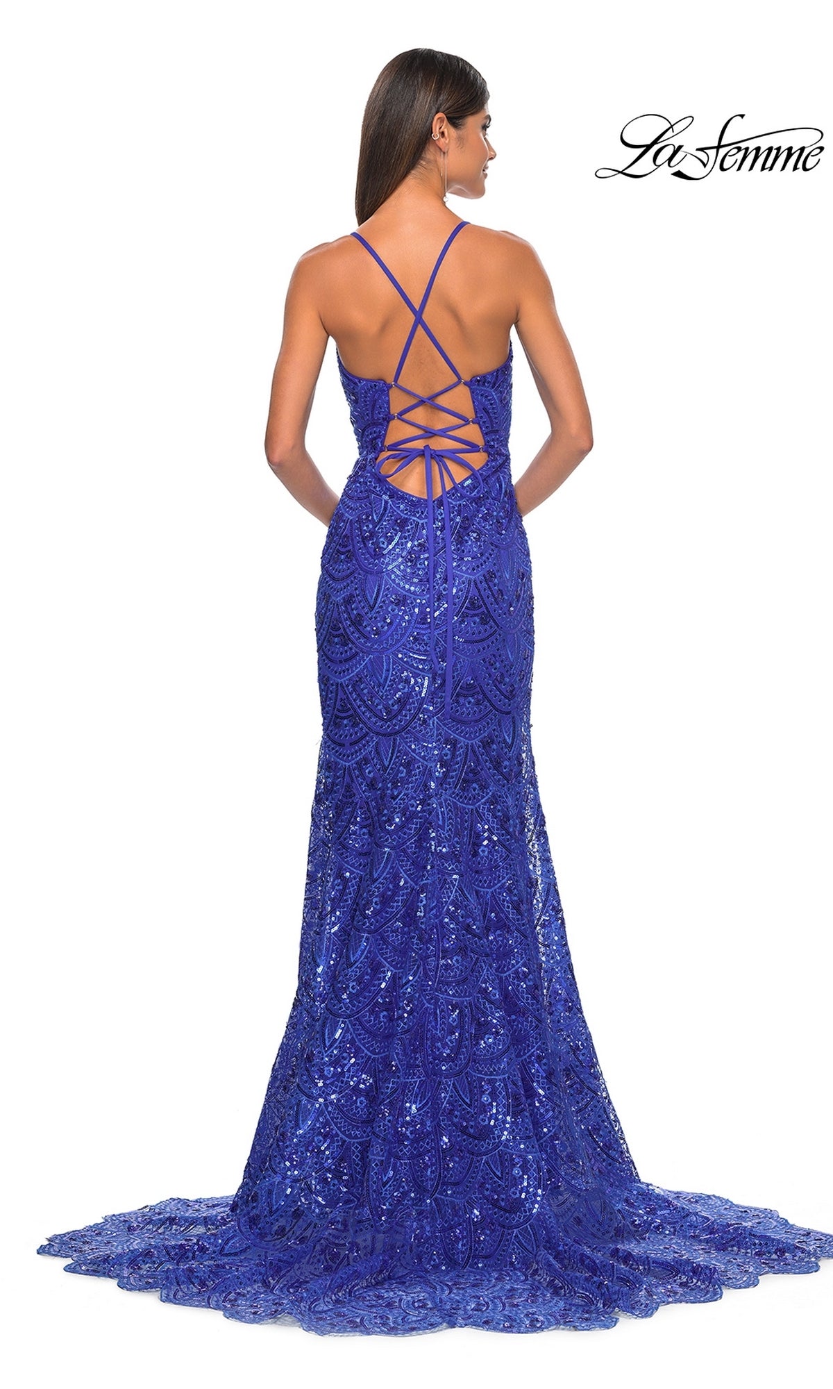 A woman stands facing away, wearing the La Femme Sequin-Print Long Prom Dress 31865 in royal blue, featuring floor-length sequins, an open strappy back, and lace-up detailing.