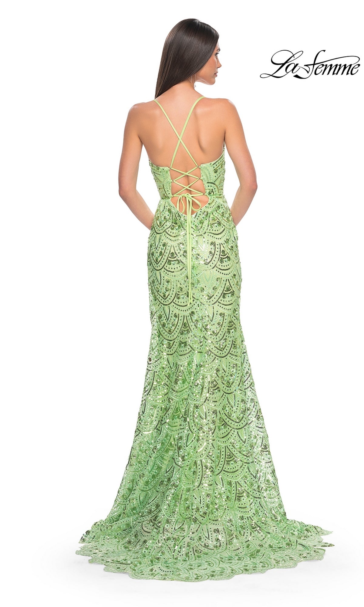 Woman in the La Femme Sequin-Print Long Prom Dress 31865, light green with lace mermaid silhouette, open back, and crisscross lacing, stands facing away from the camera.