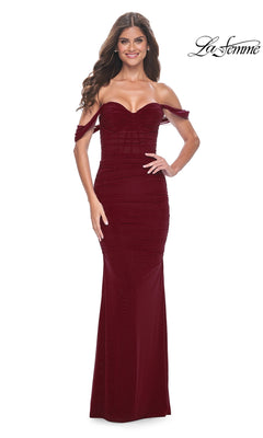 Woman in the La Femme Off-the-Shoulder Long Prom Dress 31914, a fitted burgundy gown with a sweetheart neckline, stands smiling against a white background.