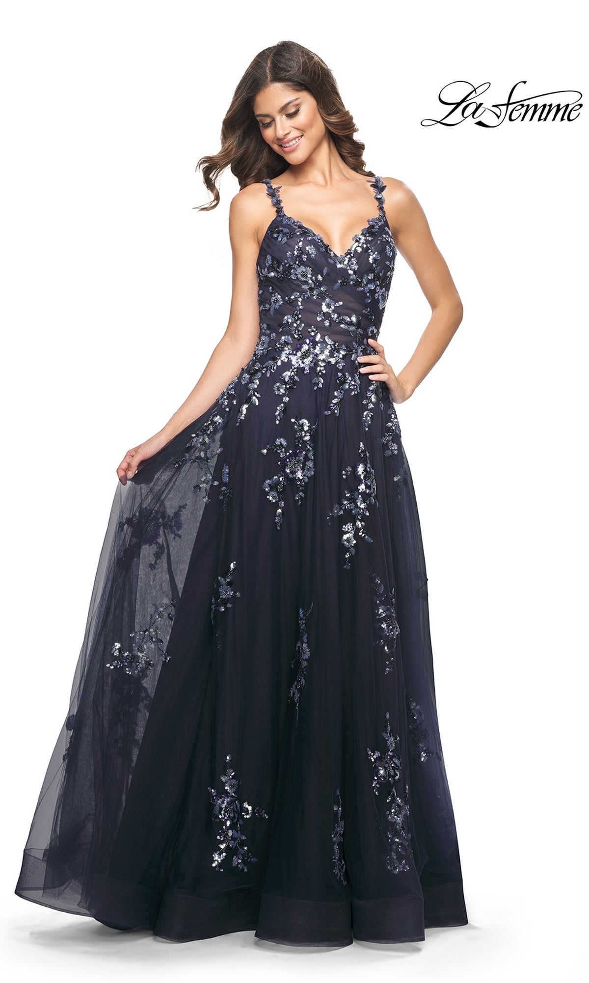 Woman in a navy blue La Femme Long Sequin-Print Prom Dress 31936, sleeveless with a full tulle skirt, posing with one hand holding the dress; 
