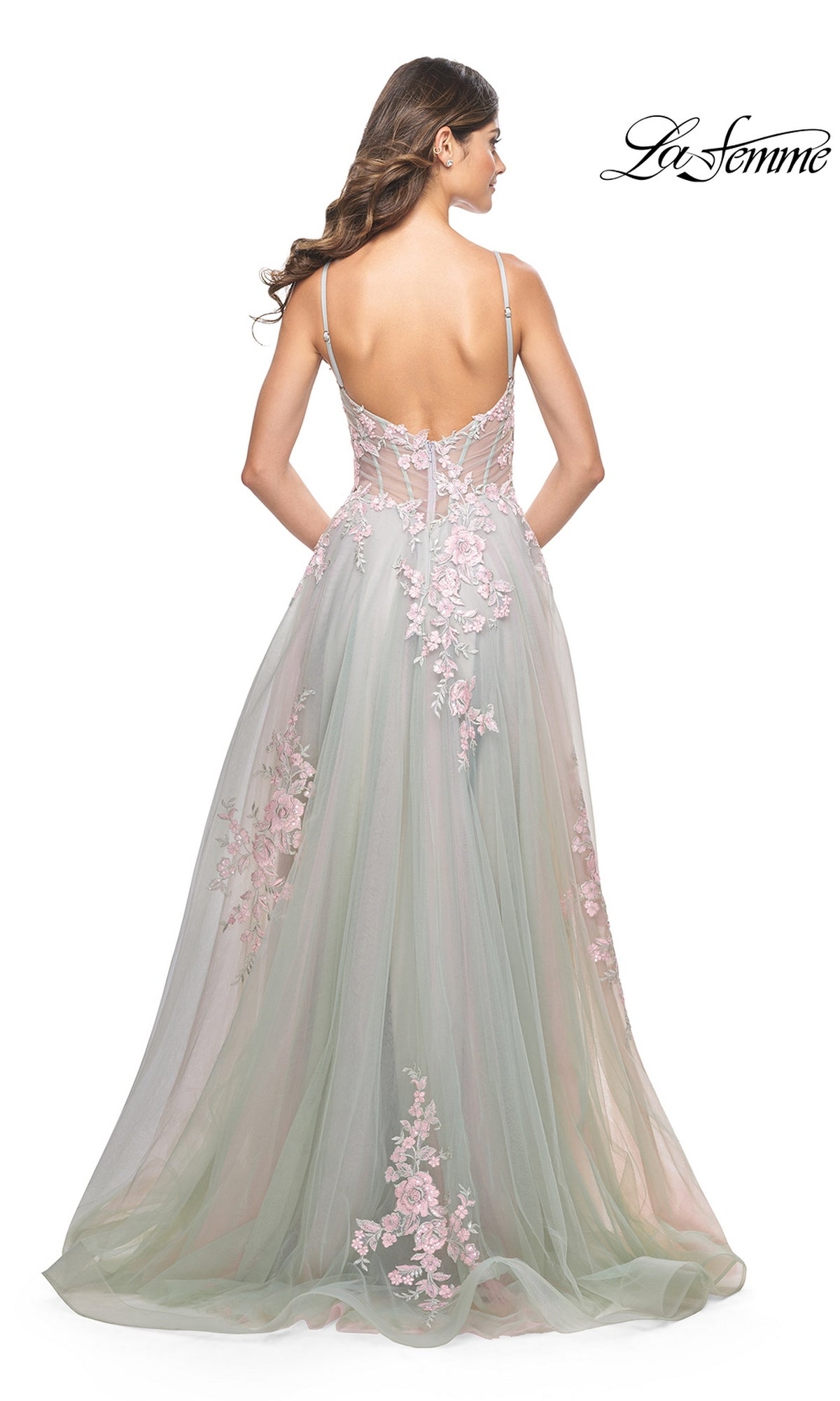 A woman stands facing away in the La Femme Embroidered-Lace Long Prom Dress 31939, featuring light green tulle with pink floral appliqués, spaghetti straps, a low back, and embroidered-lace details. 