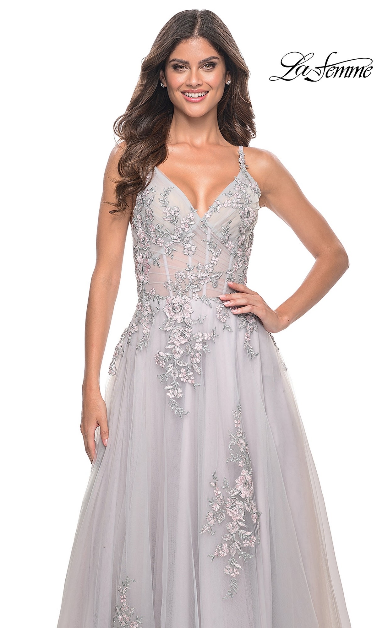 A woman stands smiling in the La Femme Embroidered-Lace Long Prom Dress 31939, a sleeveless light gray gown with sheer and lace details, against a white background featuring the 