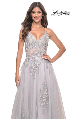 A woman stands smiling in the La Femme Embroidered-Lace Long Prom Dress 31939, a sleeveless light gray gown with sheer and lace details, against a white background featuring the "La Femme" logo.