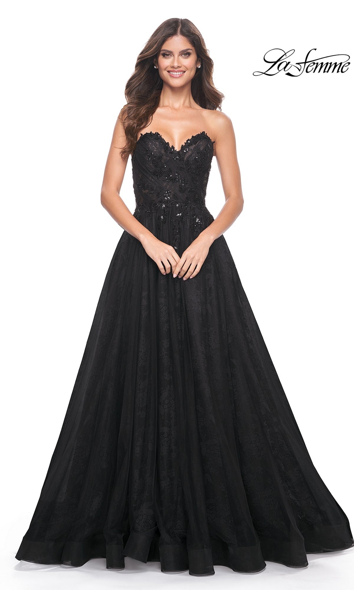 A woman models the La Femme Strapless Long Prom Ball Gown 31954, featuring lace and sequin details, smiling against a white background with the 