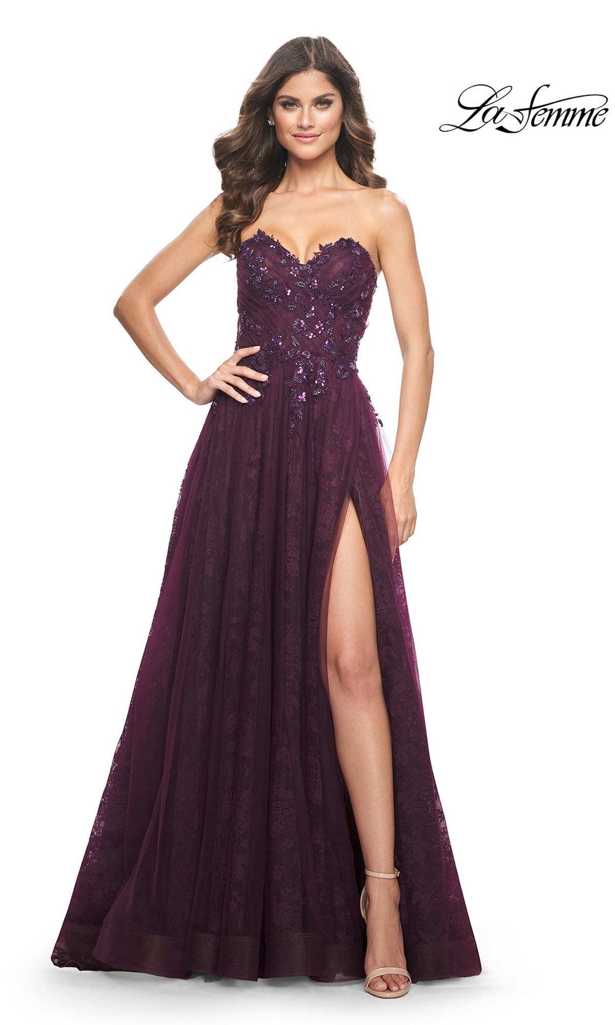 Woman in the La Femme Strapless Long Prom Ball Gown 31954, a floor-length burgundy dress with floral details and thigh-high slit, stands with one hand on her hip.