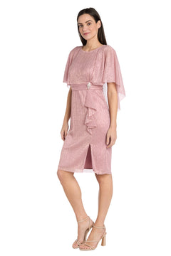 A woman models the R&M Richards 3195P caped knee-length party dress in shimmering pink with flutter sleeves and a waist detail, paired with nude heels, standing against a white background.