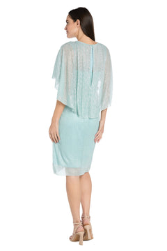 A woman stands facing away, wearing the R&M Richards 3195P Caped Knee-Length Party Dress with loose, semi-sheer sleeves and beige heeled sandals.