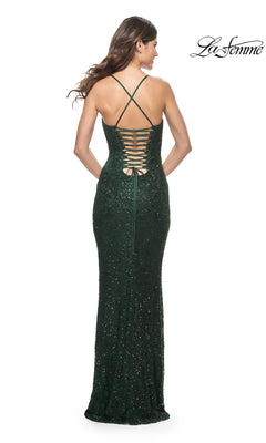 A woman models the La Femme Tight Long Beaded Prom Dress 31973 in dark green, featuring crisscross straps and a lace-up back, standing with her back to the camera.