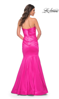 A woman models the La Femme Strapless Long Mermaid Prom Dress 31980 in hot pink, featuring a fitted, floor-length silhouette with flared hem, ruched detailing, zipper closure, and shown from the back.