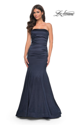 A woman models the La Femme Strapless Long Mermaid Prom Dress 31980 in navy blue with subtle bodice ruching, standing before a white background. The "La Femme" logo appears in the top right, showcasing this gorgeous designer gown.