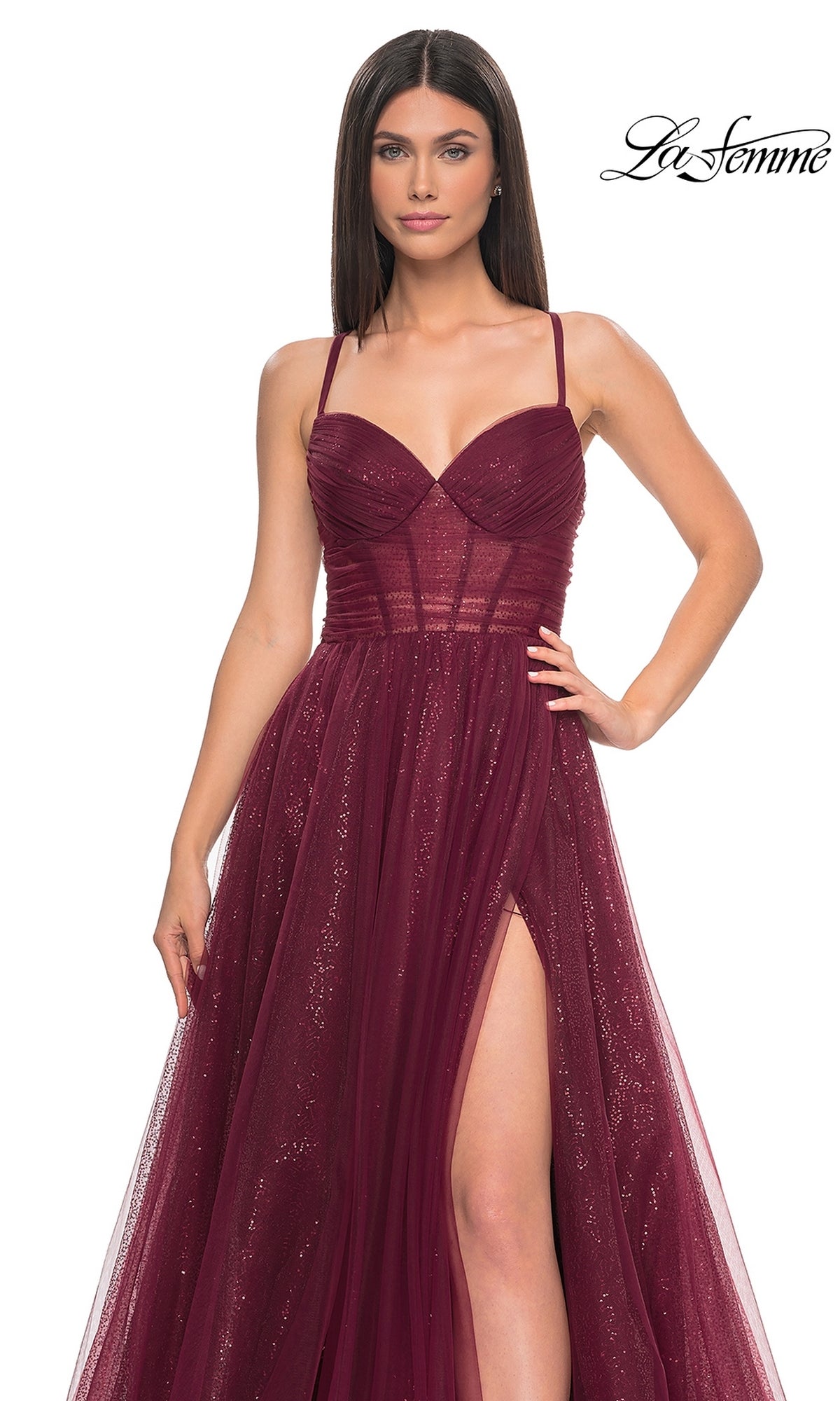 Woman in a sleeveless, deep red sequin A-line prom dress (La Femme 31986) with a sweetheart neckline, thin straps, fitted bodice, and high slit, standing against a plain background. 