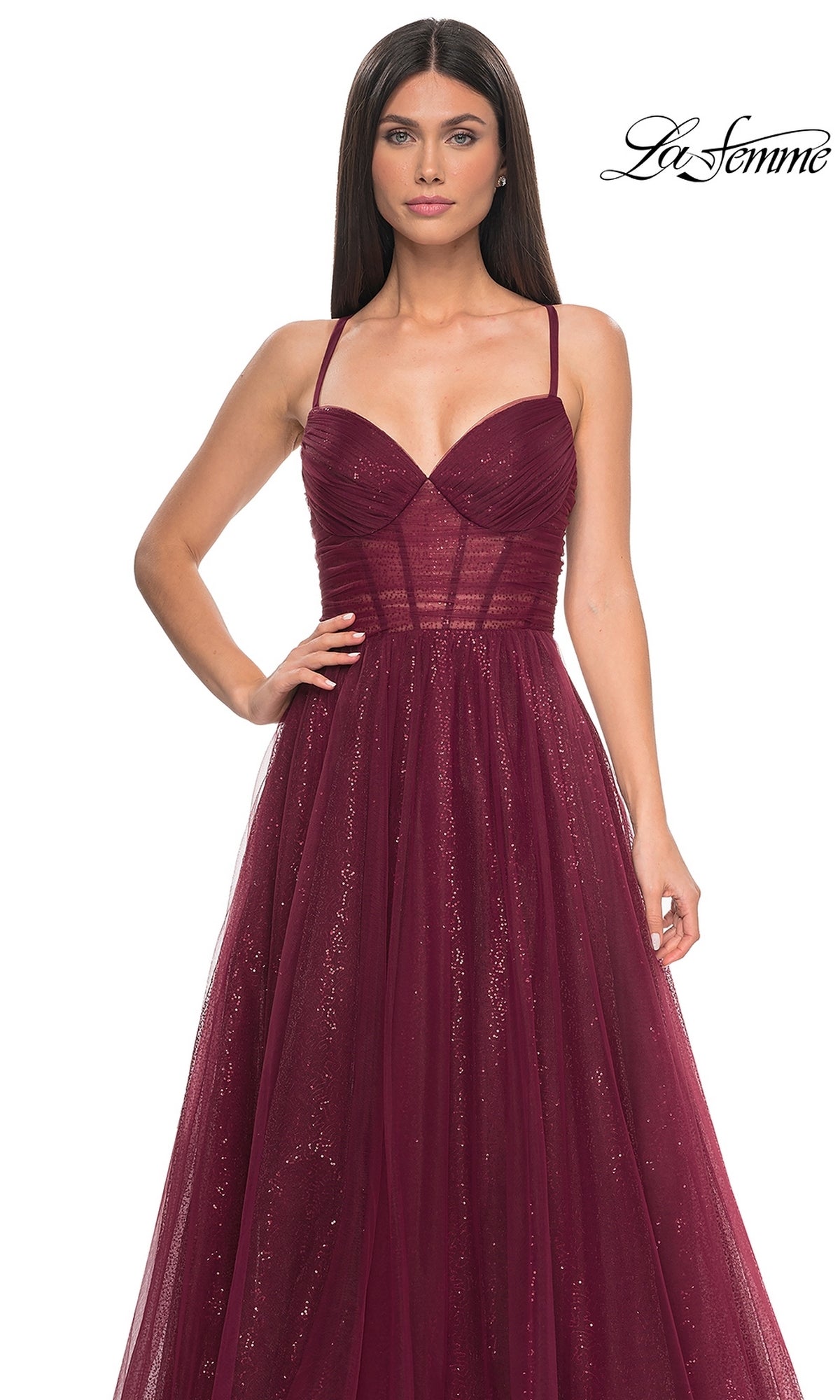 A woman wears the La Femme Long Sequin A-Line Prom Dress 31986—sleeveless, burgundy, with spaghetti straps, a fitted sheer bodice, and a flowing shimmery tulle skirt. 