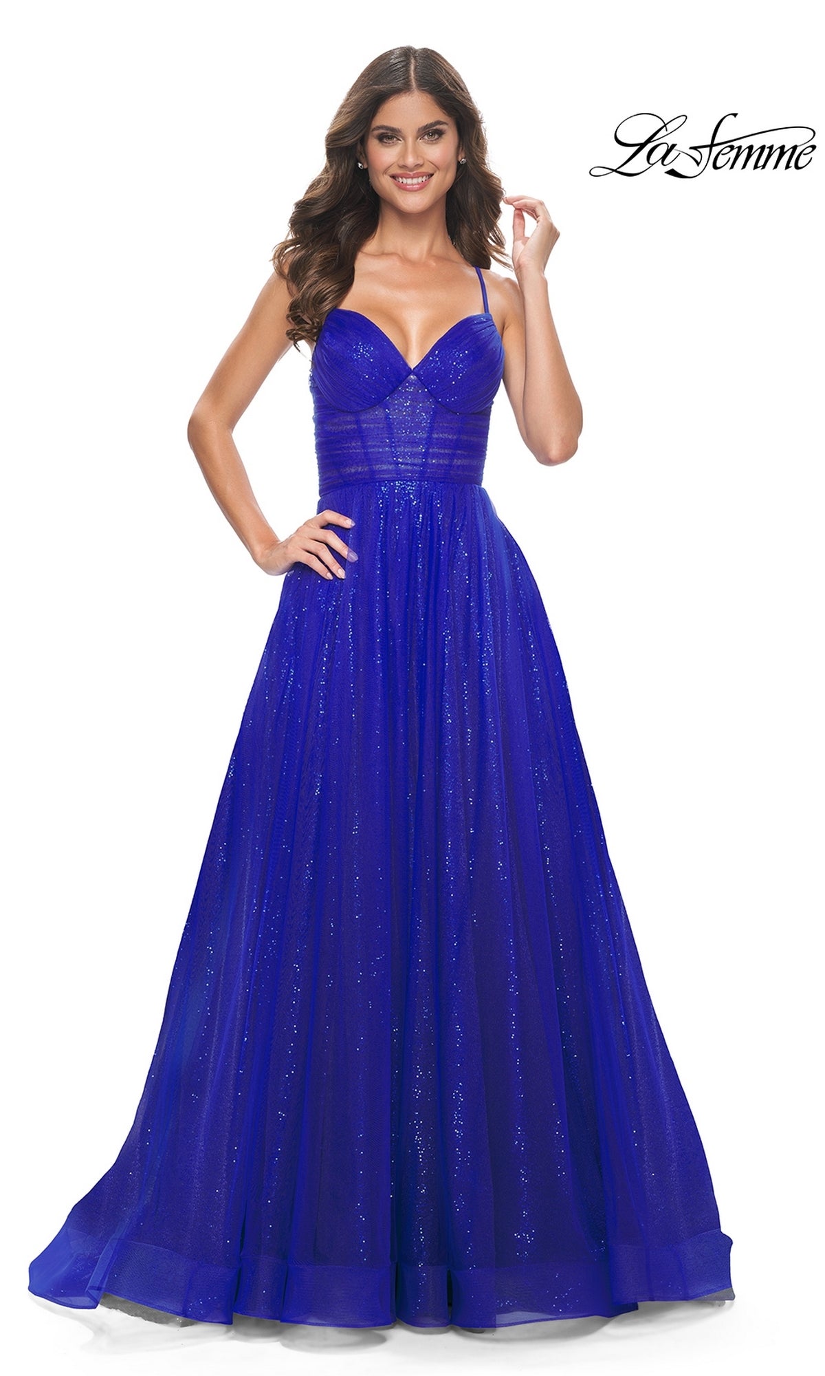 A woman wears the La Femme Long Sequin A-Line Prom Dress 31986, a floor-length royal blue gown with thin straps, fitted bodice, subtle shimmer, and full flowing skirt. 