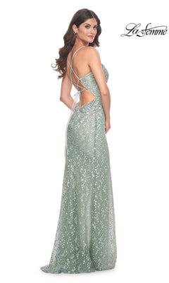 Woman in a sparkly light green Strappy-Back Long La Femme Beaded Prom Dress 31993, featuring a floor-length skirt and open strappy back, stands looking over her shoulder.