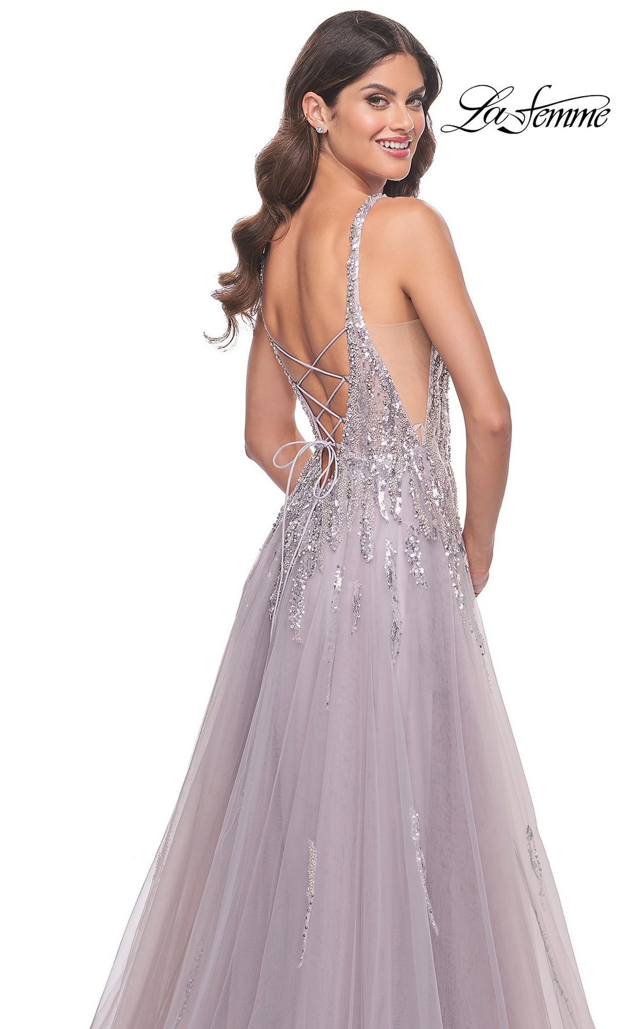 Smiling over her shoulder, a woman wears the La Femme 31995 Sequined Long Mauve Prom Dress featuring a light purple hue, A-line silhouette, lace-up back, and silver sequin embellishments.
