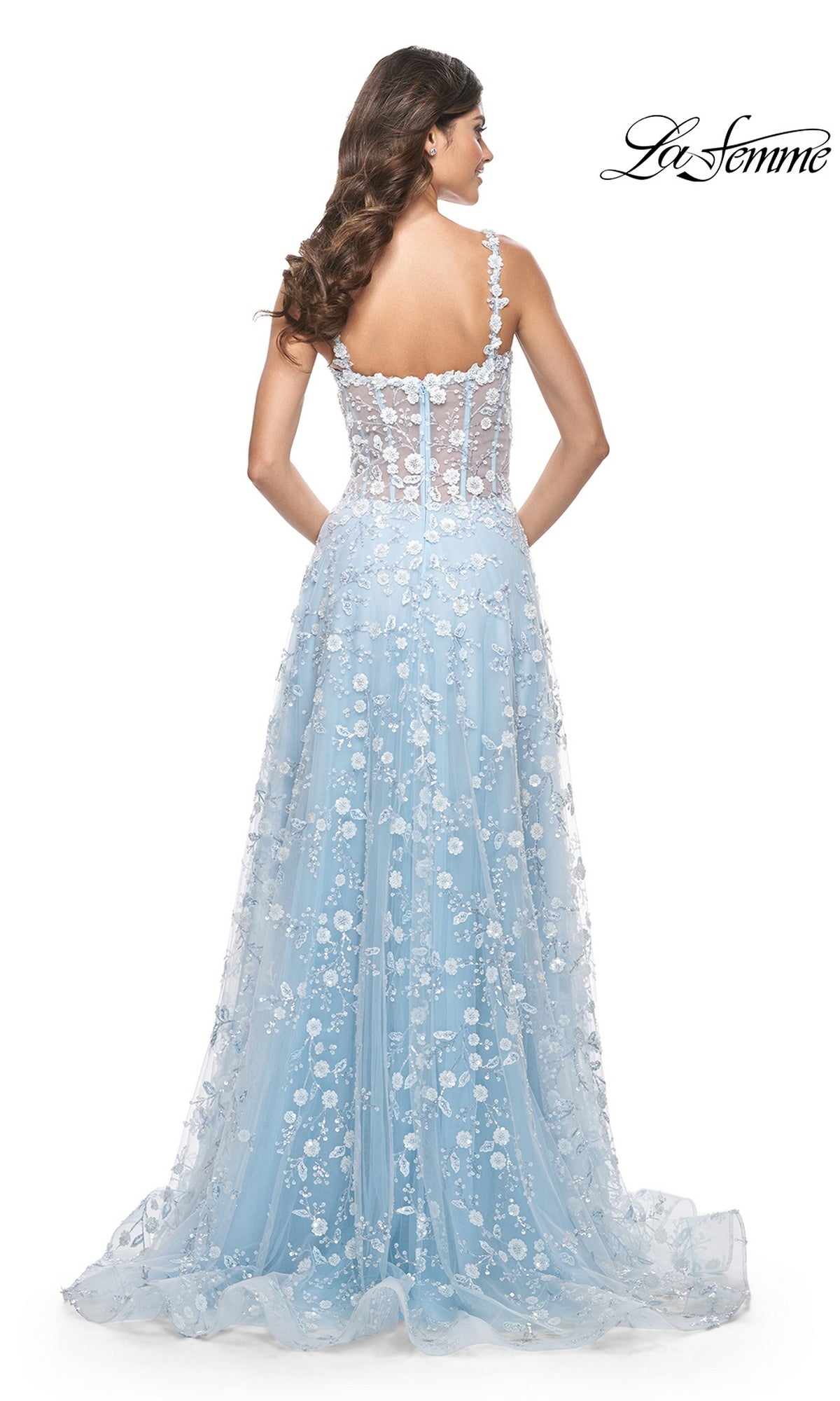 A woman in the La Femme Floral-Embellished Long Prom Dress 31996, featuring light blue fabric, floral embroidery, a sheer corset-style back, and lace A-line skirt, stands facing away. The La Femme logo appears in the top right corner.