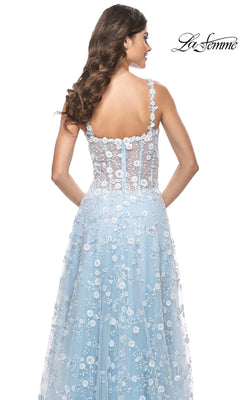 A woman with wavy brown hair wears the La Femme Floral-Embellished Long Prom Dress 31996—a light blue floral lace gown with a sheer back and spaghetti straps—standing against a white background with the "La Femme" logo in the top right.