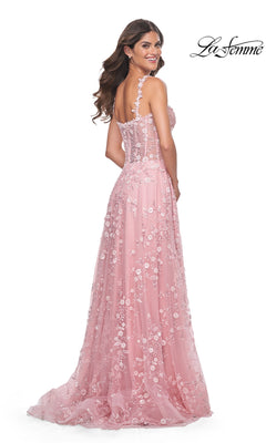 A woman faces backward and smiles in the La Femme Floral-Embellished Long Prom Dress 31996, a sheer pink gown with floral accents. "La Femme" appears in the top right corner.