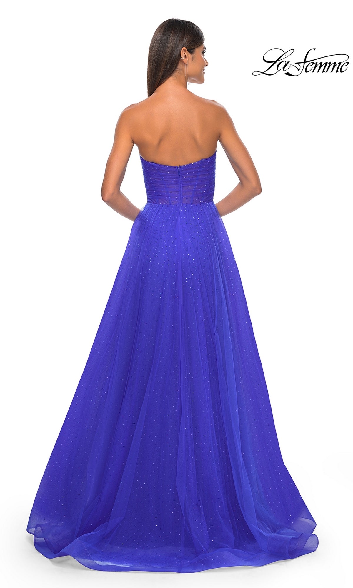 A woman stands facing away, wearing the La Femme Strapless Long Prom Ball Gown 31997 in royal blue, featuring a fitted bodice and subtly sparkly, full flowing A-line skirt for an elegant formal look.