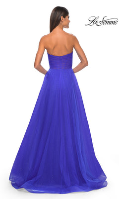 A woman stands facing away, wearing the La Femme Strapless Long Prom Ball Gown 31997 in royal blue, featuring a fitted bodice and subtly sparkly, full flowing A-line skirt for an elegant formal look.