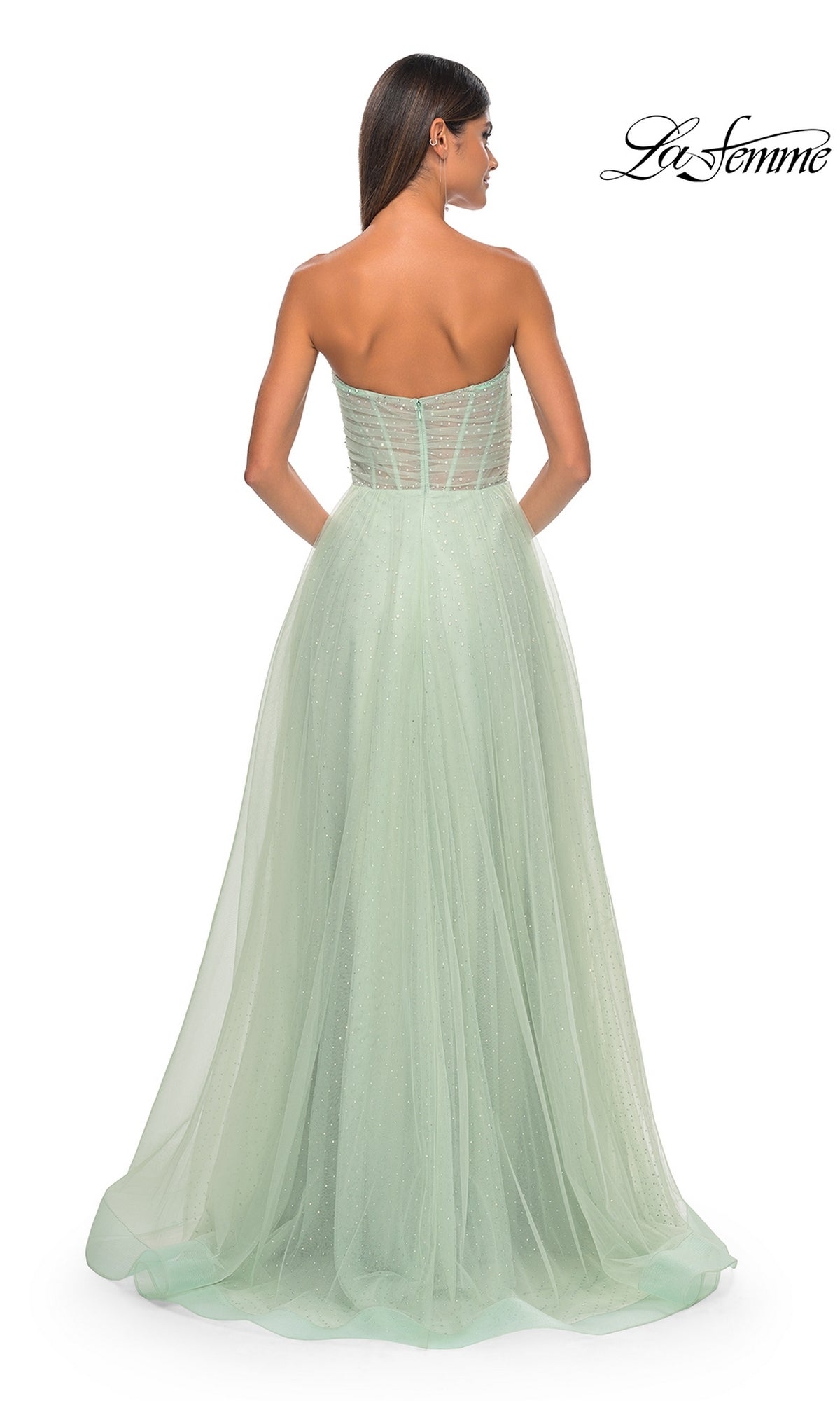 A woman models the La Femme Strapless Long Prom Ball Gown 31997, a light green, floor-length A-line dress with a sheer tulle overlay, shown from the back against a white background.