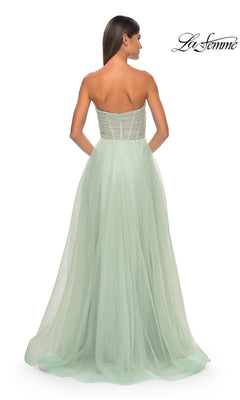 A woman models the La Femme Strapless Long Prom Ball Gown 31997, a light green, floor-length A-line dress with a sheer tulle overlay, shown from the back against a white background.
