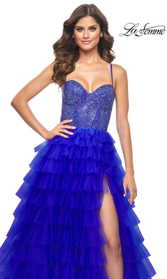 A woman models the La Femme Long Ruffled Prom Ball Gown 32002, featuring a blue a-line design with sequined bodice, spaghetti straps, and high slit, standing against a white background with the "La Femme" logo in the top right.