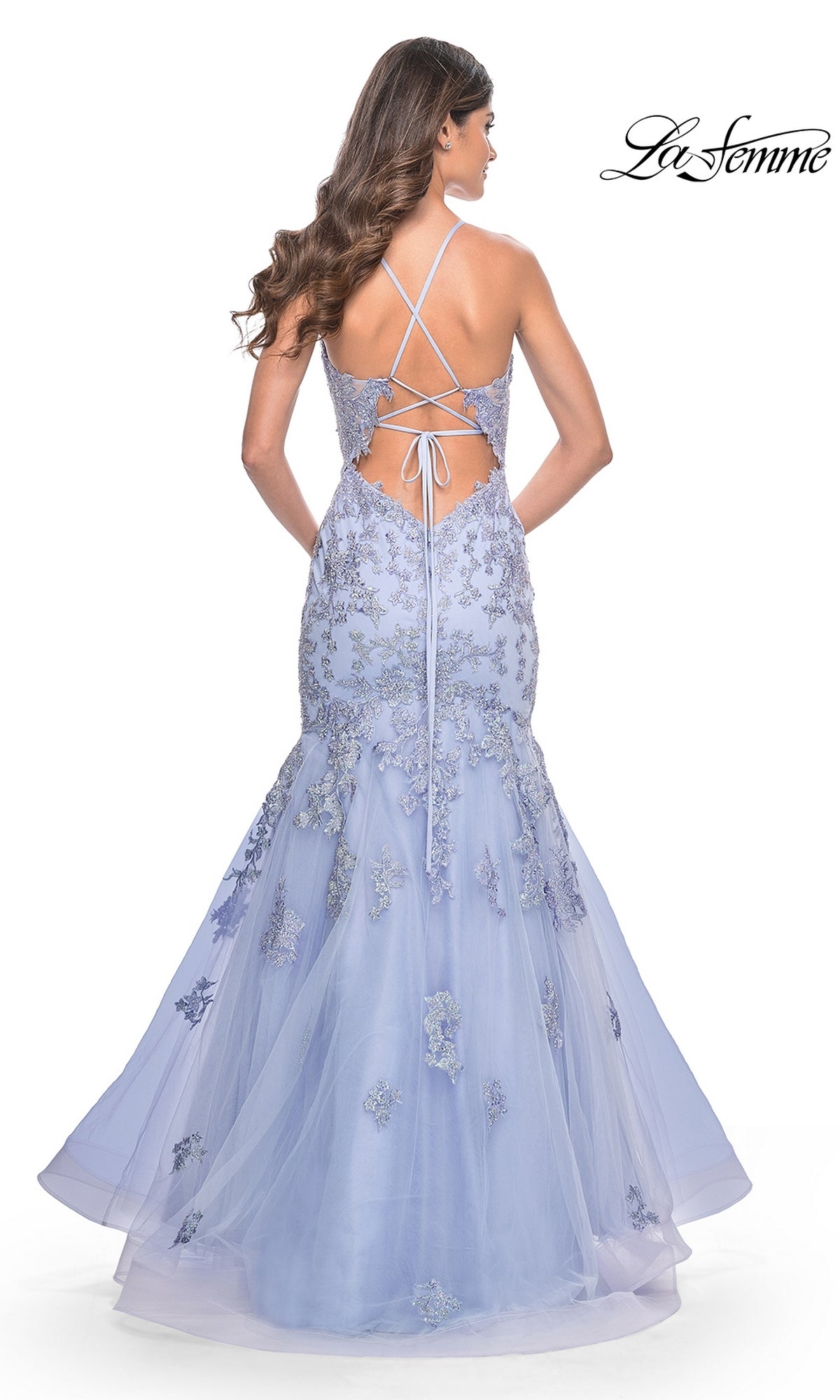 A woman models the La Femme Long Lace Mermaid Prom Dress 32004, featuring lavender lace applique, a tulle mermaid skirt, and a crisscross open back. The 