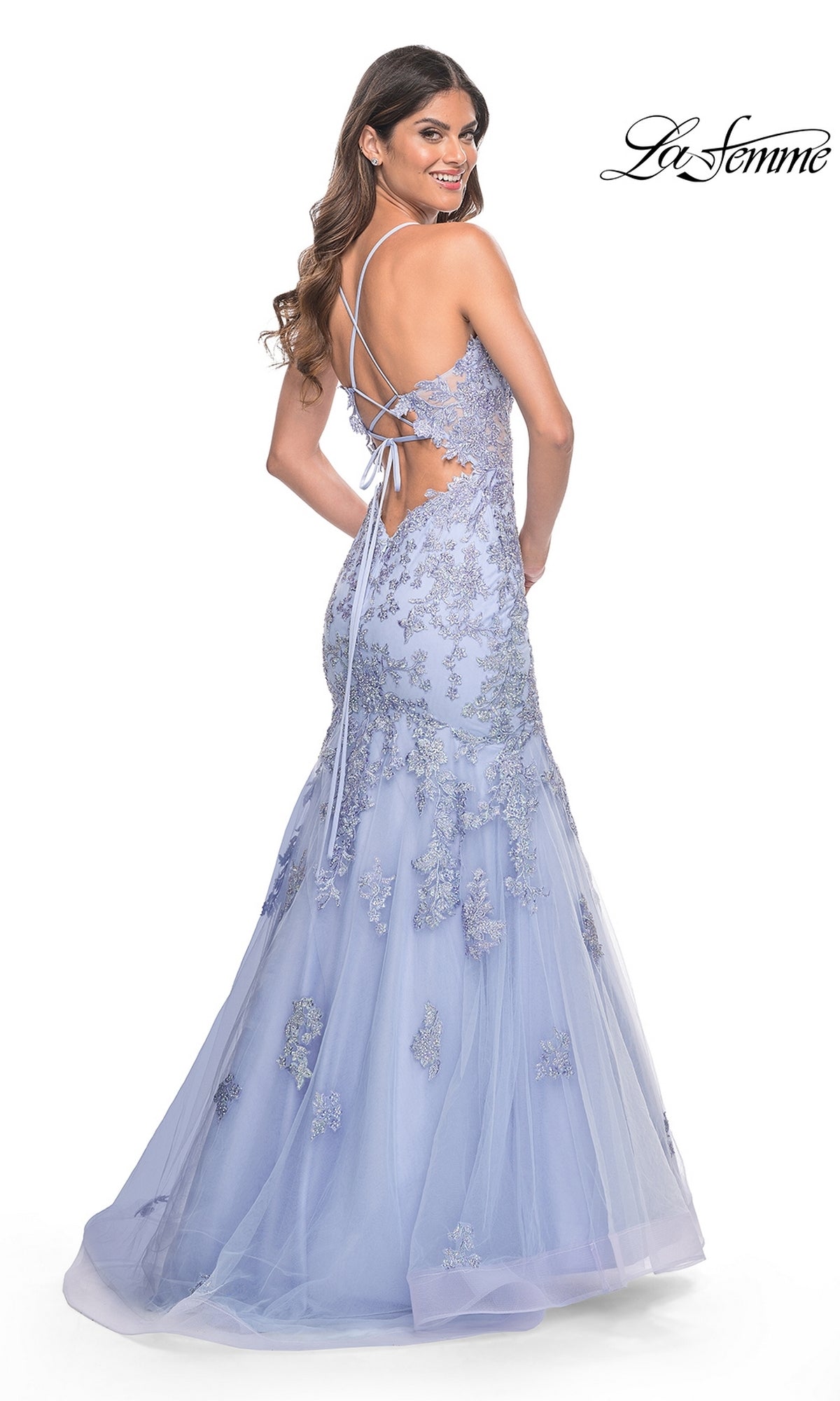 A woman poses elegantly over her shoulder in the La Femme Long Lace Mermaid Prom Dress 32004, featuring lavender lace appliqué, an open back, and crisscross tie detail.