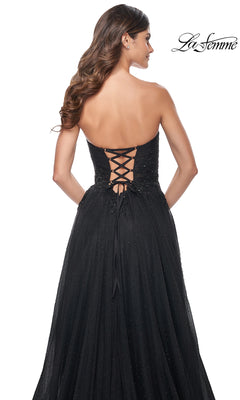 Woman stands with her back to the camera in the La Femme Long Black Strapless Prom Dress 32005, featuring a lace-up back, subtle sparkles, and a flowing skirt for an elegant, unforgettable look.
