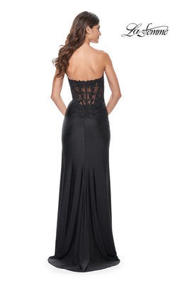 A woman with long wavy hair models the La Femme Sheer-Waist Strapless Long Prom Dress 32011, a black, floor-length gown with a sheer-lace bodice and subtle embellishments. The La Femme logo appears in the top right corner.
