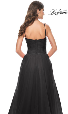 A woman with long wavy hair models the La Femme Sheer-Waist Long Prom Ball Gown 32017, a black, strapless A-line dress with a fitted bodice and flowing skirt, shown from the back. The La Femme logo appears in the top right corner.