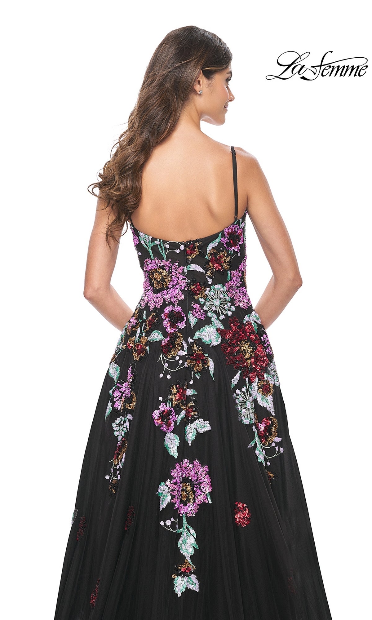 A woman with long brown hair models the La Femme Sequin-Floral Long Prom Dress 32019—a black, sleeveless gown with colorful floral embroidery—seen from the back on a white background.