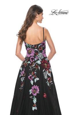 A woman with long brown hair models the La Femme Sequin-Floral Long Prom Dress 32019—a black, sleeveless gown with colorful floral embroidery—seen from the back on a white background.