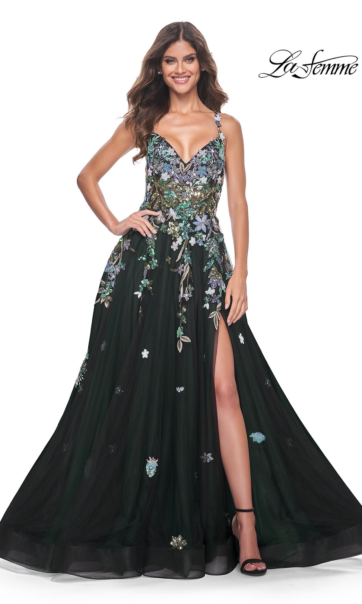 A woman stands smiling in the La Femme Sequin Flower-Print Long Prom Dress 32023, featuring black fabric, sequin floral embroidery, spaghetti straps, a deep neckline, and a thigh-high slit. La Femme logo appears in the corner.